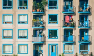 Elegancka loggia i balkon z niebieskimi ramami okiennymi, pełne zieleni i suszącego się prania, tworzą kolorowy kontrast z betonową fasadą.
