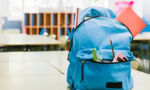 Niebieski plecak z przyborami szkolnymi: linijka, zeszyt, długopisy, ołówek i kalkulator.