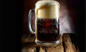 Boccale di birra scura con schiuma abbondante, forse la birra americana più famosa, su un tavolo di legno rustico.