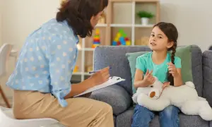 Psychoterapeutka rozmawia z dziewczynką trzymającą misia w gabinecie.