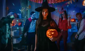 Kiedy obchodzi się Halloween, młoda kobieta w stroju czarownicy trzyma świecącą dynię na imprezie z przyjaciółmi w kostiumach.