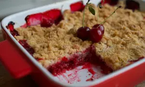 Un délicieux crumble fruits rouges, garni de cerises fraîches, sort du four.