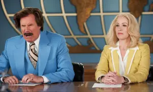 Man i blå kostym grimaserar, tecken på att du håller på att få sparken. Bredvid sitter en kvinna i gul kavaj lugnt.