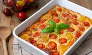 Un délicieux clafoutis tomates cerises, doré et garni de basilic frais, prêt à être dégusté.