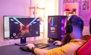 Gamer mit Headset spielt am PC. Die leuchtende Grafik auf dem Monitor und der beleuchtete PC-Tower deuten auf die Vorteile eines Twitch Partners hin.