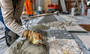 Un ouvrier applique du mortier pour un ragréage de sol. Des tas de sable et de ciment sont prêts pour le travail.