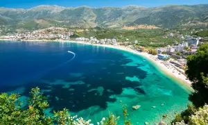 Malownicze wybrzeże riwiera albańska z turkusową wodą, piaszczystą plażą i górami w tle.