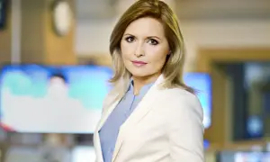 Agnieszka Gozdyra w białej marynarce i niebieskiej koszuli, w tle ekrany telewizyjne. Czy Agnieszka Gozdyra ma dzieci? Tego nie widać na zdjęciu.