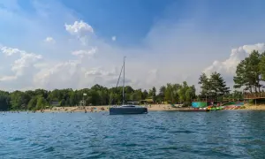 Żaglówka cumuje przy piaszczystej plaży nad jeziorem Głębocko Opolskie. Ludzie odpoczywają i kąpią się w słoneczny dzień.