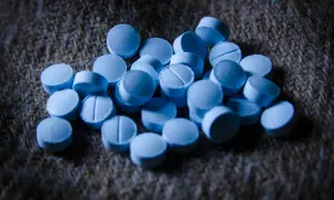 En hög med blå tabletter, som kan associeras med bensodiazepiner biverkningar, ligger på en grov, brun yta.