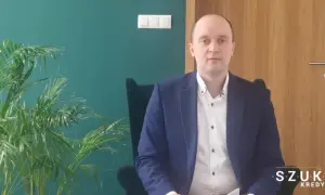 Mężczyzna w garniturze siedzi w fotelu obok rośliny.