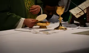 Kapłan trzyma hostię nad złotą pateną. Obok kielich i księga liturgiczna. To obrazuje przyczyny zmian w tekstach modlitw w nowym mszale rzymskim.