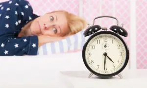 Mujer en pijama mira un despertador, su expresión refleja la **intención paradójica** de querer dormir pero no poder.