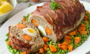 Ein saftiger falscher Hase, umwickelt mit Speck, serviert auf Erbsen und Karotten.