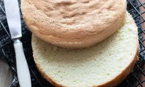 Due dischi di pan di spagna senza glutine, uno sopra l'altro, su una griglia. Un coltello è visibile a sinistra.