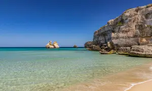 Acque cristalline e scogliere imponenti definiscono la spiaggia più bella del Salento. Faraglioni emergono dal mare turchese, un vero paradiso.