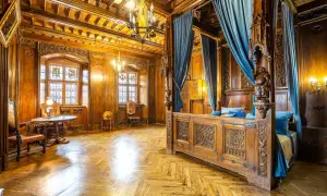 Luksusowe noclegi zamek Czocha: bogato zdobiona sypialnia z baldachimem, witrażami i drewnianymi panelami.