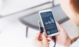 Kobieta podłącza pendrive do smartfona, pokazując, jak włączyć funkcję OTG. Na ekranie telefonu widoczny wykres i tekst.