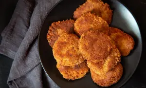 Un piatto nero pieno di dorate polpette di verdure, croccanti fuori e morbide dentro, pronte per essere gustate.