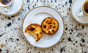 Dwa pyszne pastel de nata na talerzyku, obok filiżanki kawy. Idealny deser na każdą porę dnia.