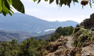 Sendero rocoso con vistas a montañas y un embalse, ideal para rutas senderismo Alpujarra.