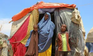 En kvinna och två barn står framför ett provisoriskt boende i Somalia. Deras historia är en del av Somalias historia.