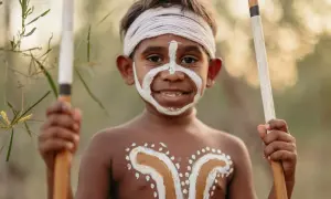 Giovane membro del popolo australiano con pittura facciale e corporea tradizionale, impugna lance.
