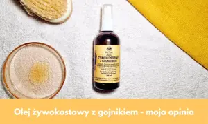 Olej żywokostowy z gojnikiem w buteleczce z atomizerem, obok kieliszka z płynem i szczotki do masażu. Naturalna pielęgnacja.