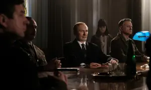 W nowym filmie Vegi, mężczyźni w mundurach i garniturze siedzą przy stole.