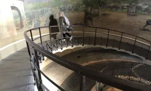 Una persona sale la scala a chiocciola all'interno della torre di San Martino, con un affresco di battaglia che decora le pareti.
