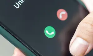 Dłoń zbliża się do ekranu telefonu, by odebrać połączenie od nieznanego numeru. Słychać lekki echo w telefonie.