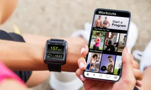 Une personne utilise son smartphone pour apprendre comment régler une montre connectée smartwatch, affichant des entraînements et des données de fitness.