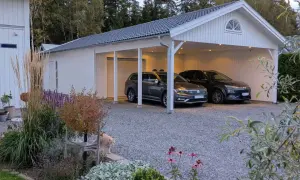 Vitt garage med två bilar under taket. En katt smyger i rabatten framför. Perfekt för att bygga garageport.