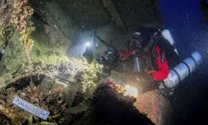 Nurkowie badają wrak statku, być może **Britannic**, z kamerą i oświetleniem. Widoczne są szczątki, muszle i ciemne głębiny.