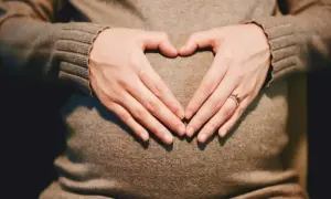 Dłonie tworzą serce na twardym brzuchu w ciąży. Widać obrączkę na palcu.