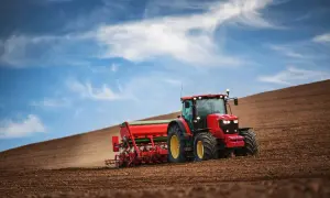 Czerwony traktor z siewnikiem orze pole. To obrazek z kategorii "prawo jazdy" kategorii T, pokazujący pracę w rolnictwie.