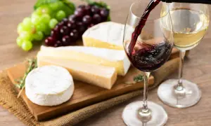 Un bicchiere di vino rosso viene versato, accanto a formaggi assortiti e grappoli d'uva. L'abbinamento perfetto di vino per formaggi.