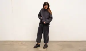 Kobieta w ciemnoszarym, welurowym komplecie dresowym z czerwonym logo. Luźne spodnie z marszczeniem przy kostkach i oversize'owa bluza tworzą modne stylizacje z dresami.