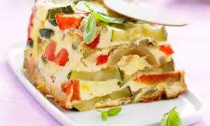 Tranche de terrine de légumes colorée, avec courgettes, poivrons rouges et une touche de basilic frais.