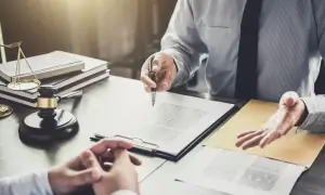 Prawnik omawia z klientką kwestie dziedziczenia po mężu z dziećmi. Na biurku widać młotek sędziowski i wagę sprawiedliwości.