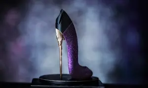 Elegancka, fioletowa, brokatowa carolina herrera szpilka z ozdobnym, złotym obcasem, prezentowana na ciemnej podstawie.