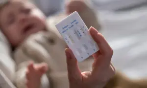 Dłoń trzyma test combo, który wykrywa wirus RSV, grypę i COVID-19. W tle niewyraźne dziecko.