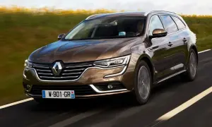 Brązowe renault talisman kombi pędzi po drodze, mijając pola.