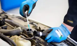 Mekaniker kontrollerar glykol i bilen med en refraktometer. Blå handskar skyddar händerna.