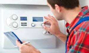 Tecnico regola la temperatura acqua sanitaria su una caldaia, con appunti in mano.