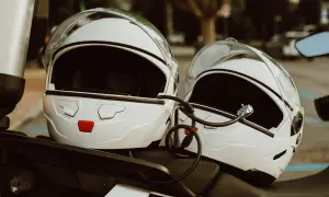 Dwa białe kaski motocyklowe połączone linką zabezpieczającą. Mocowanie kasku do motocykla zapewnia bezpieczeństwo podczas postoju.