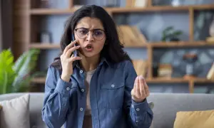 Donna con occhiali parla al telefono con espressione frustrata, un gesto della mano che suggerisce il desiderio di chiudere il telefono in faccia psicologia.