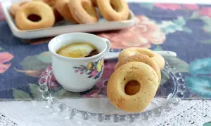 Biscotti senza burro dorati su un piattino di vetro, accanto a una tazza di tè con limone.