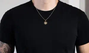 Un hombre luce un colgante sol oro con detalles intrincados sobre una camiseta negra.