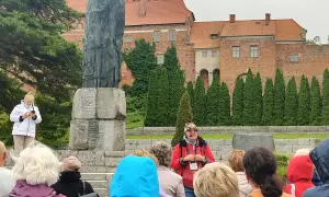 Wycieczka po Fromborku: przewodnik opowiada o Koperniku przy pomniku, w tle katedra. Atrakcje Fromborka odkrywane przez turystów.